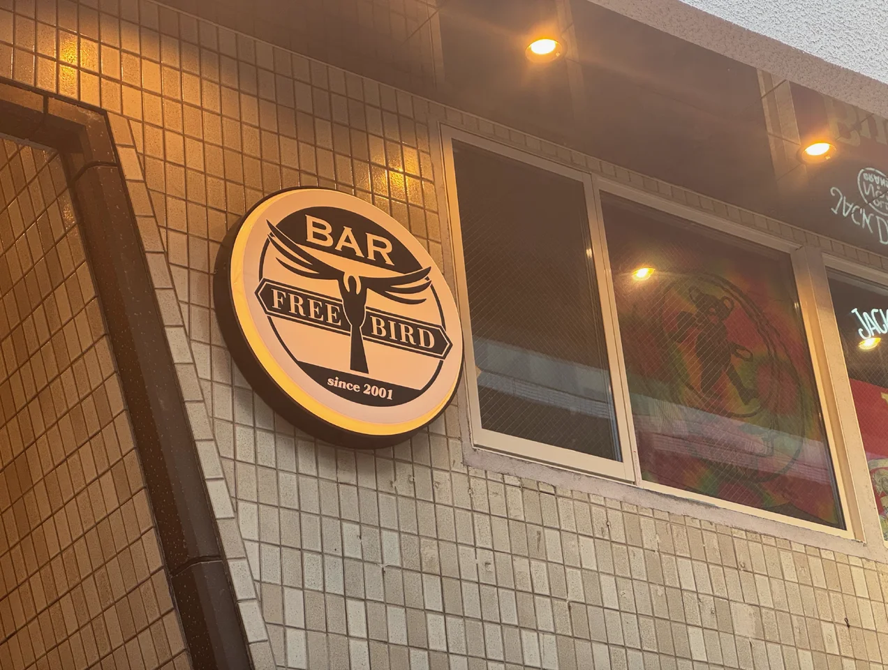 暖色照明の下で店舗外壁に設置されたFREE BIRDの円形看板